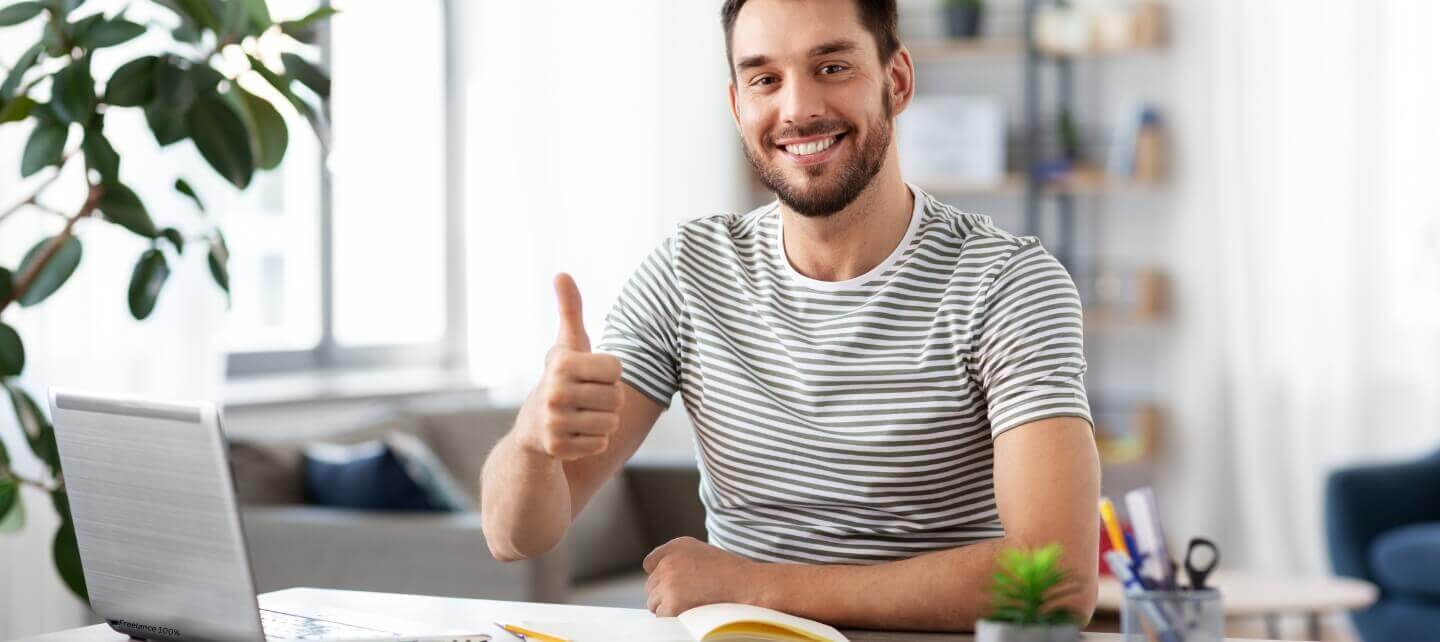 Smiling freelancer giving a thumbs up while working on a laptop at home.