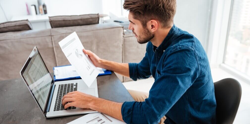 Entrepreneur reviewing reports on laptop and paper