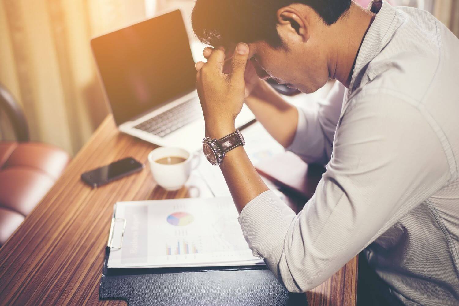 Stressed looking Asian man at laptop surrounded by paperwork