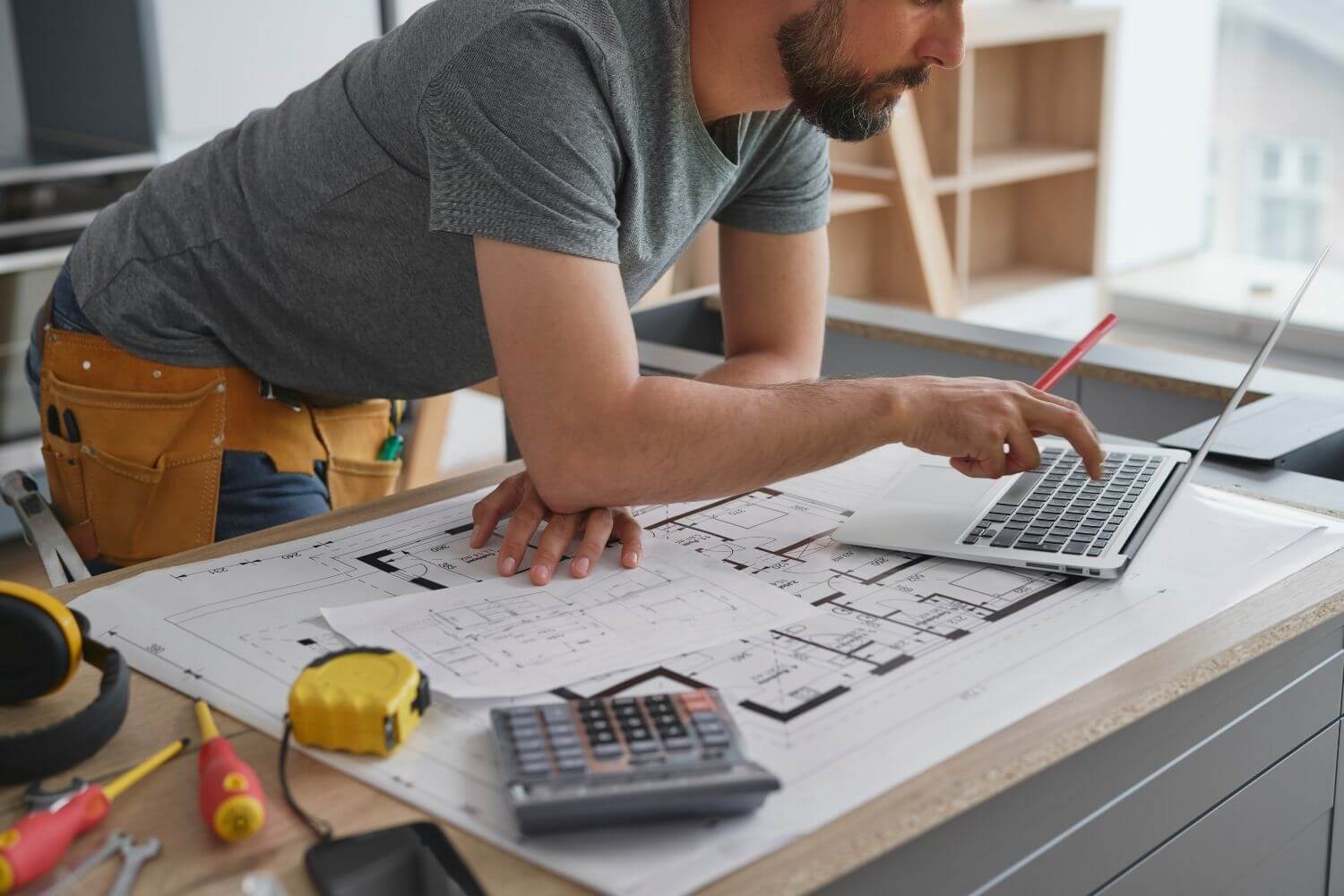Construction worker works on a laptop surrounded by architects building plans and tools