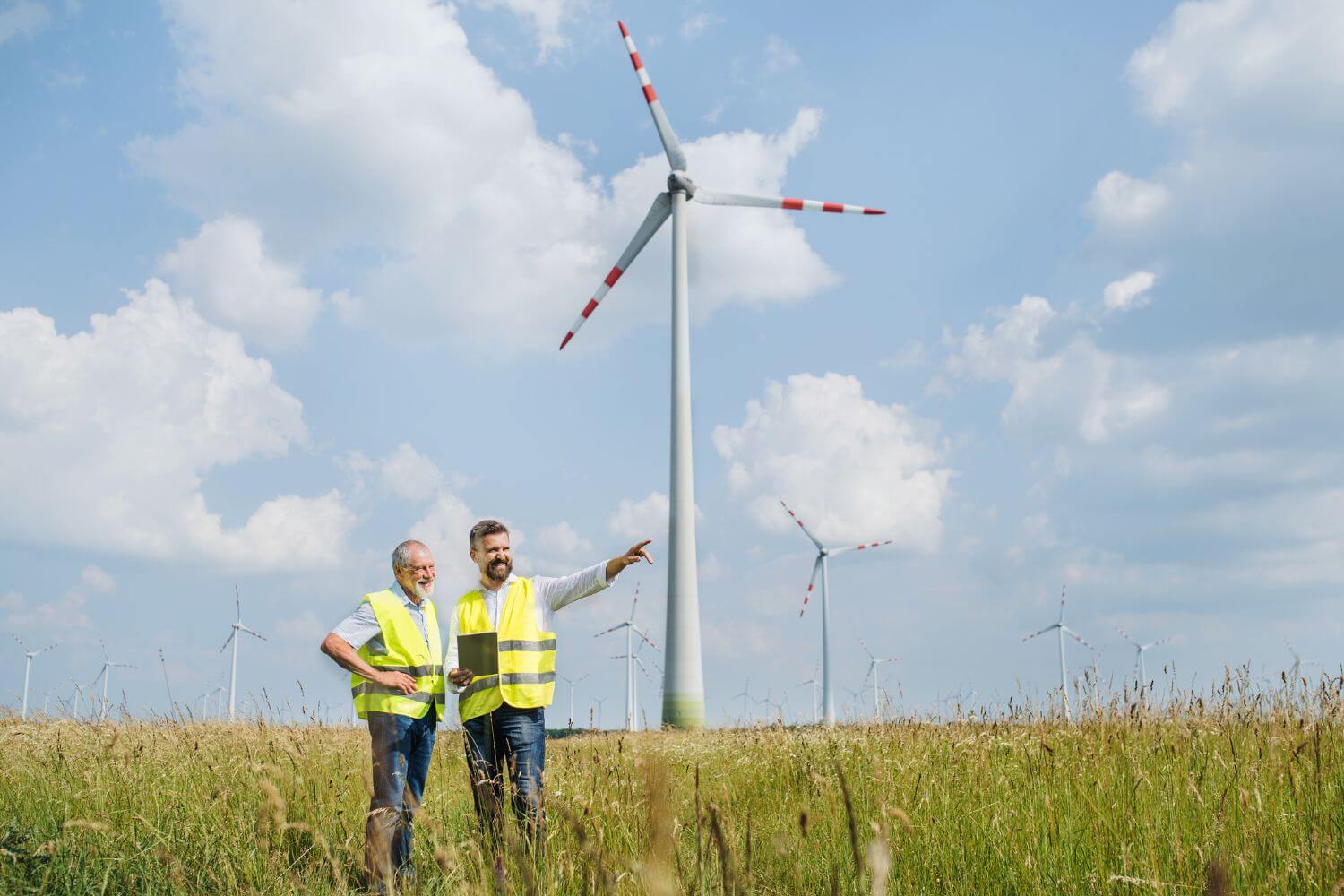 Two male workers wearing high visibility vests in front of a wind farm