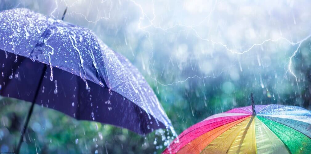 Two umbrellas in a rainstorm with lightning overhead, symbolising the protection business insurance provides from sudden risks.