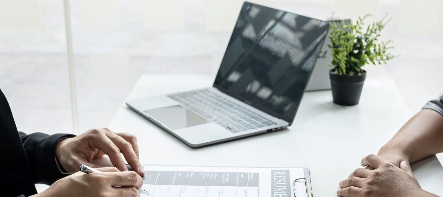Recruiter reviewing a candidate's resume during an IT job interview with a laptop on the desk, reflecting hiring trends and IR35 offset impact.