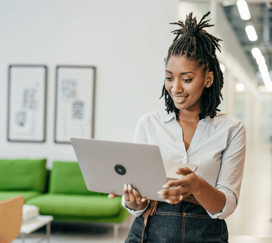Woman stood in an office looks happily at her laptop