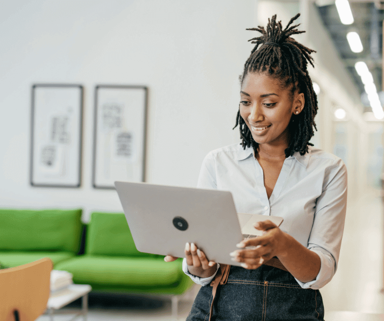 Woman stood in an office looks happily at her laptop