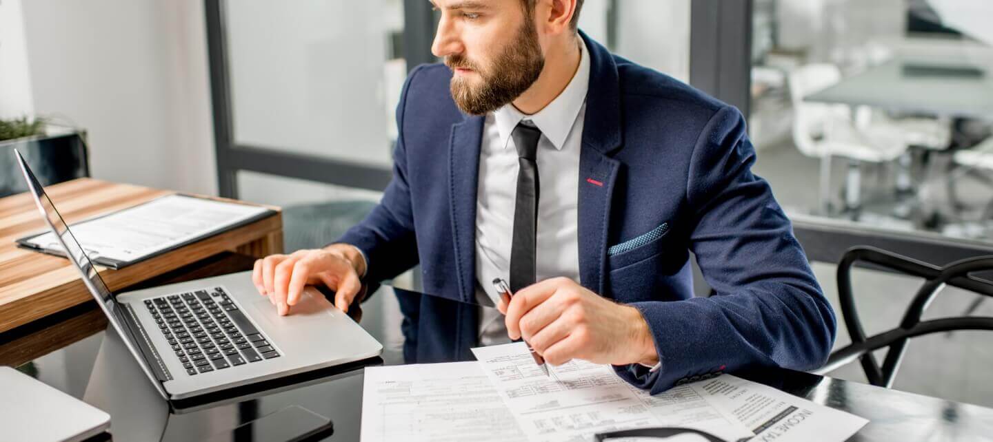 Professional contractor in a suit reviewing tax documents and working on a laptop, considering IR35 status and Employer NI implications.