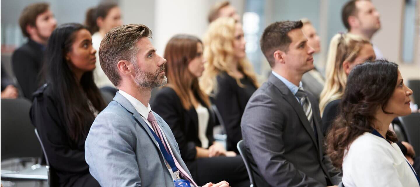 Business professionals attentively listening at an IR35 conference, dressed in formal attire, representing contractors and recruiters discussing off-payroll working rules.