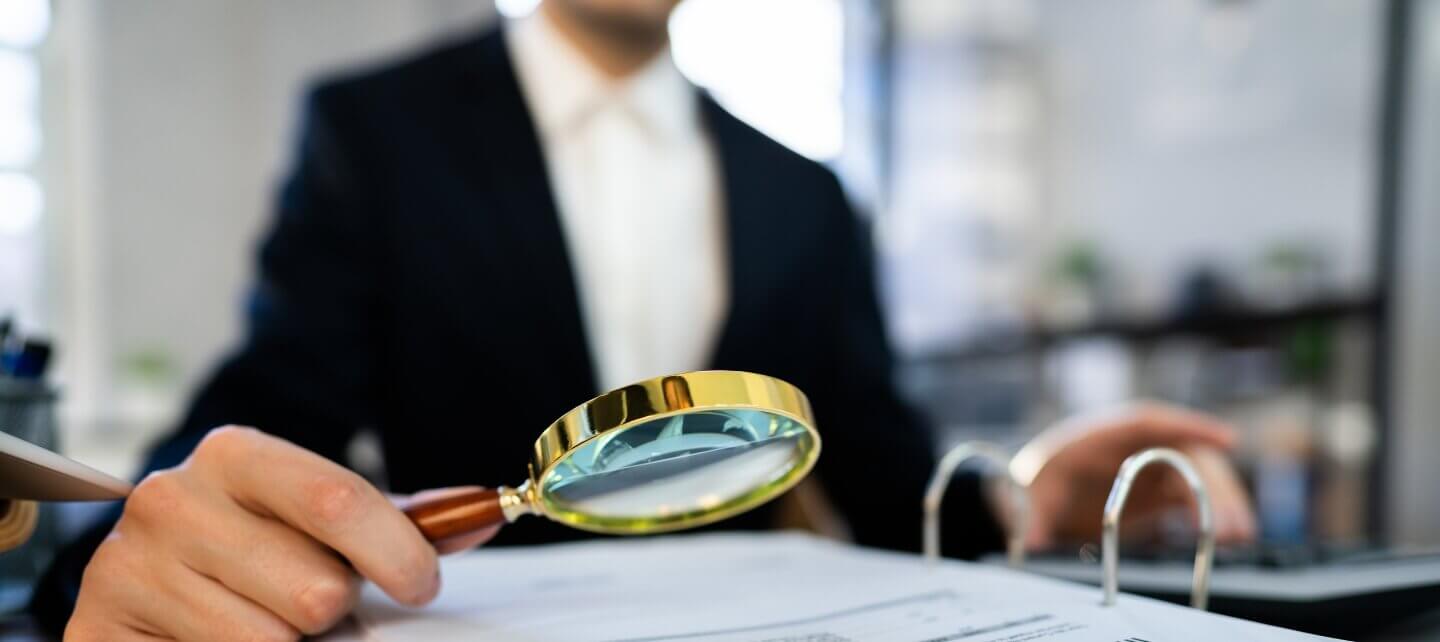 Business professional examining legal documents with a magnifying glass, symbolising an IR35 investigation and tax scrutiny.