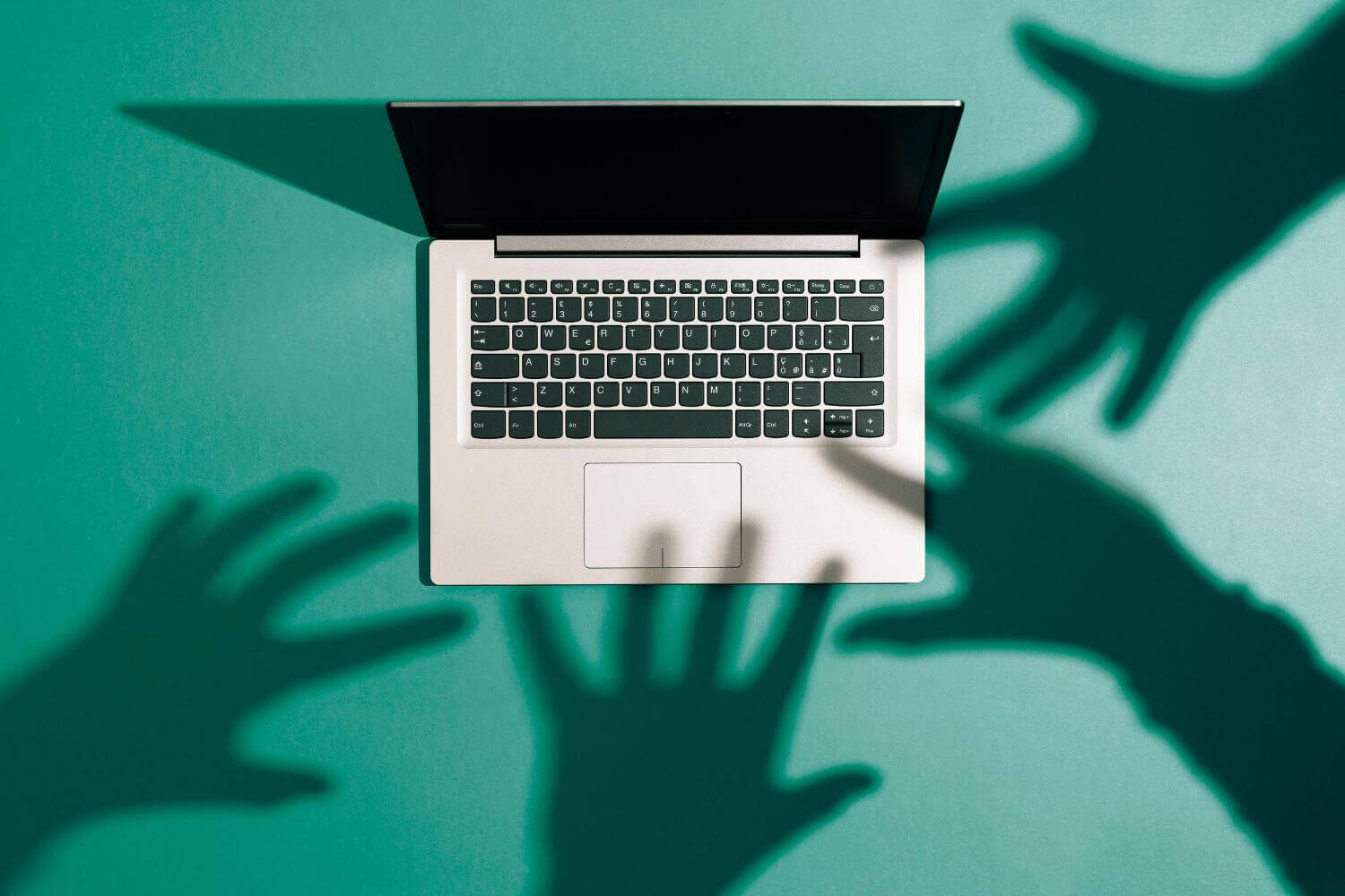 Image of shadow hands reaching for a personal laptop, representing a step-by-step guide on what to do if you're a cyber attack victim.