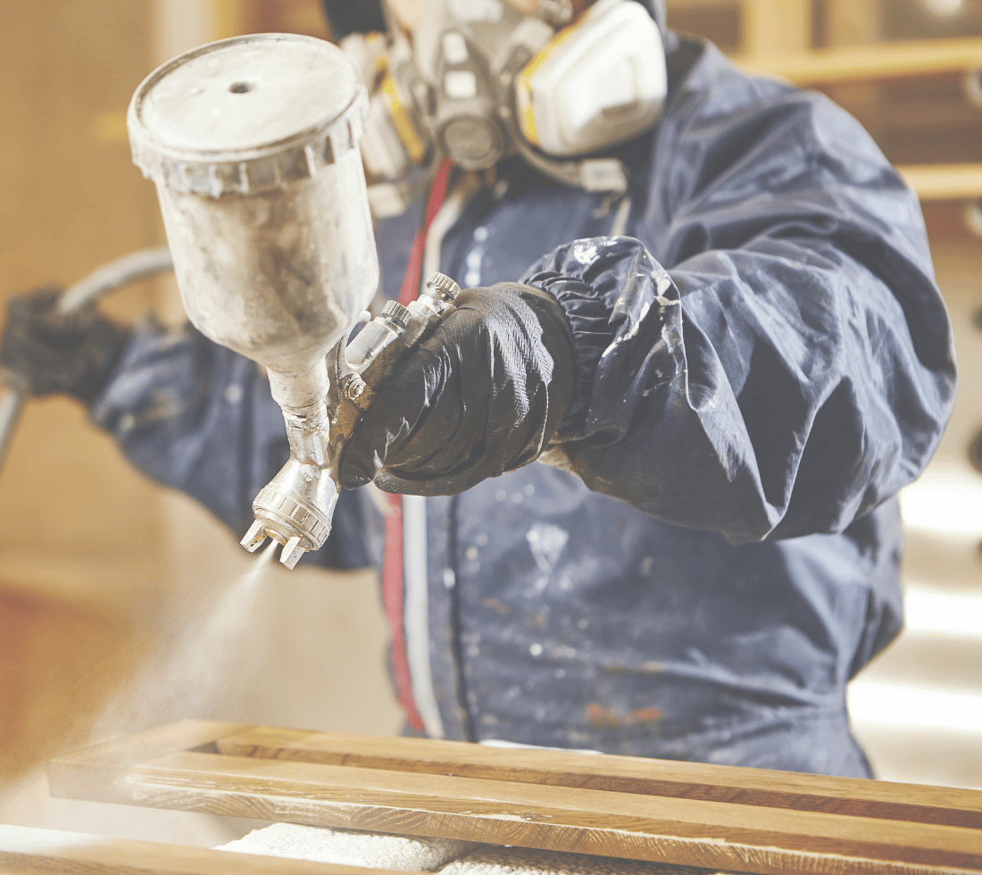 Worker wearing protective clothing whilst spraying kitchen cabinets